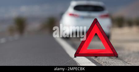 Broken down car with warning triangle behind it waiting for assistance to arrive, red triangle of a car on the road Stock Photo