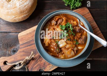 Brown beef stew with cabbage and vegetables. Served with homemade ciabatta bread on wooden table Stock Photo