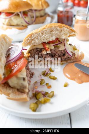 Homemade hamburger, cheeseburger or burger cut in half on a plate with burger sauce on kitchen table Stock Photo