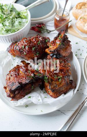 Barbecue Pork ribs with barbecue sauce and onions with salad and bread on kitchen table background Stock Photo