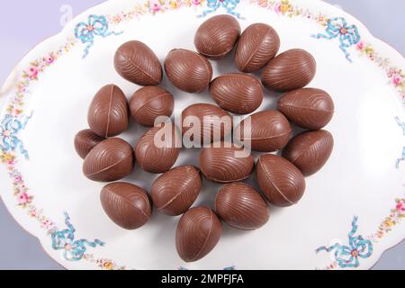 Group of Chocolate Easter eggs on a white plate with traditional decorations of bows and flowers and a pale background. Stock Photo