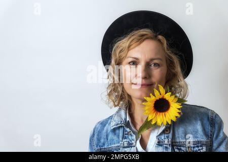 Portrait of  smiling  middle age woman with  black hat and sunflower on the light background. Stock Photo