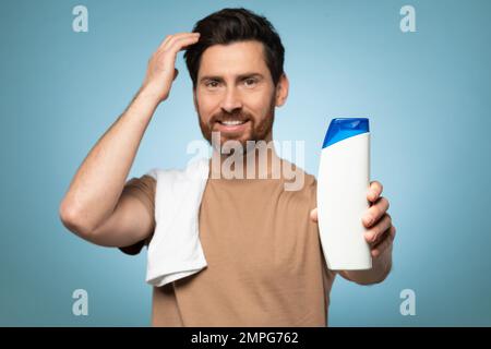 My choice. Handsome bearded man ready to take shower, standing with towel on shoulder, focus on bottle Stock Photo
