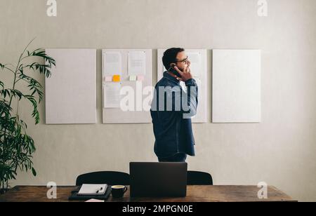 Young businessman talking on the phone while standing behind his desk in a creative office. businessman communicating with his clients while working r Stock Photo