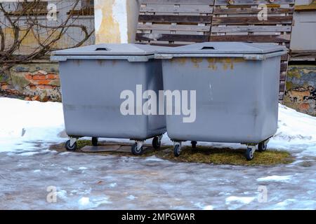 Plastic large trash cans with lids and trash inside against an orange brick wall. Large gray plastic trash cans on a city street. Waste containers. Re Stock Photo