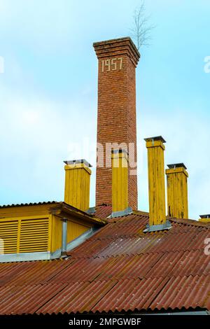 The roof of an old house with many chimneys. Many small wooden chimneys and one large one made of bricks with a year number. Stock Photo