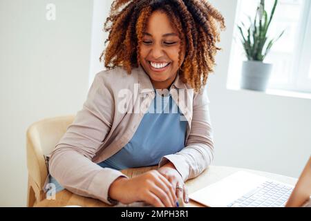 Young African American woman is working on a laptop. Focused female student is looking at computer screen and watching webinar or doing video chat by Stock Photo