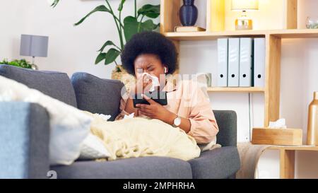 Sick afro woman streaming on phone while coughing, suffering from covid fatigue and blowing her nose with tissue. Young woman watching movies on Stock Photo