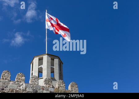 Georgian national flag (five-cross flag) waving on the wind against clear blue sky at the top of ancient watchtower of Akhaltsikhe (Rabati) Castle. Stock Photo