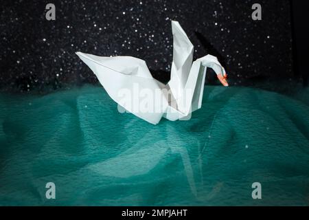 White paper origami swan on green dark background, soft focus close up Stock Photo