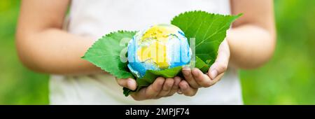 Little girl holding small planet in hands against spring or summer green background. Horizontal banner for web design. Ecology, environment and Earth Stock Photo