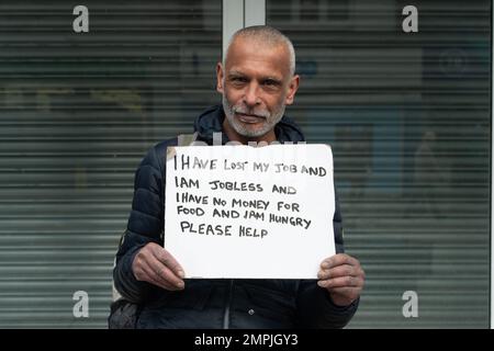 Slough, Berkshire, UK. 31st January, 2023. A homeless man who has lost his job and is homeless holds up a sign in Slough High Street asking passers by for help. Credit: Maureen McLean/Alamy Live News Stock Photo