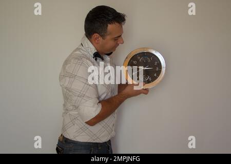 Image of a man holding a wall clock while setting the correct time. Stock Photo
