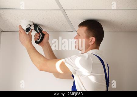 Technician installing CCTV camera on ceiling indoors Stock Photo