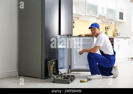 Male technician with screwdriver repairing refrigerator in kitchen Stock Photo