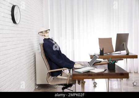 Human skeleton in suit using laptop at table in office Stock Photo