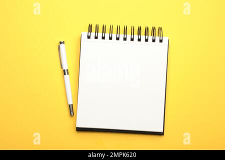 Stylish open notebook and pen on yellow background, top view Stock Photo