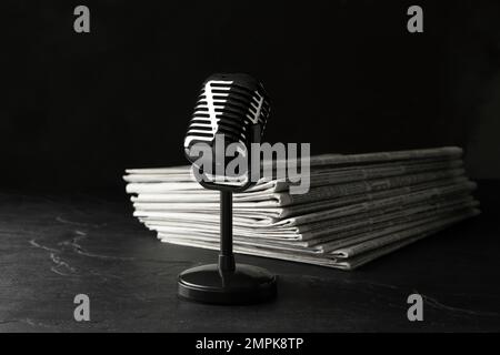 Newspapers and vintage microphone on dark stone table. Journalist's work Stock Photo