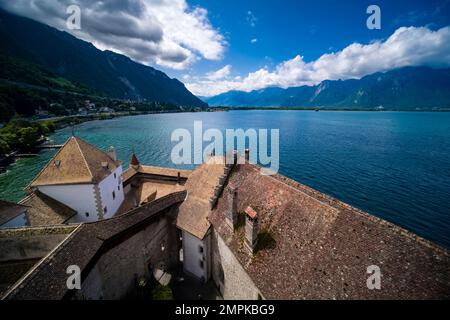 View over Lake Geneva and alpine scenery in the distance over the roofs of Chillon Castle, Château de Chillon. Stock Photo