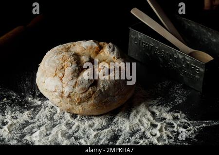 Traditional Freshly baked homemade loaf Bread, with flour and alluminium box near by on dark background. Artisan sourdough rye, wholegrain bread. Clos Stock Photo