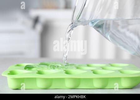 Pouring water into ice cube tray on table, closeup Stock Photo