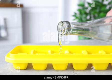 Pouring water into ice cube tray on table, closeup Stock Photo