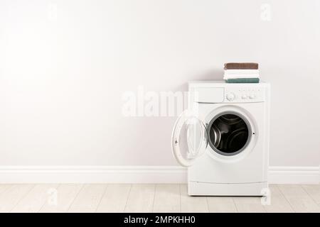 Modern washing machine with stack of towels near white wall, space for text. Laundry day Stock Photo