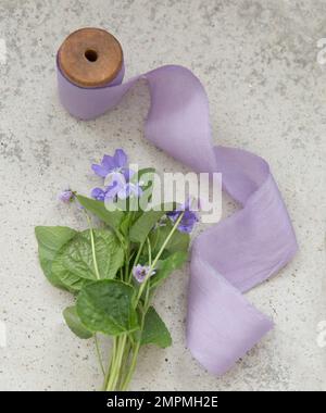 Purple silk ribbon and lillac flowers on concrete background Stock Photo