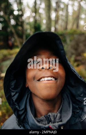Thoughtful boy looking away wearing raincoat in forest Stock Photo