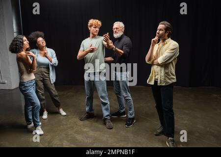 mature art director assisting redhead man during rehearsing near emotional interracial actors. Translation of tattoo: kanji, danger Stock Photo