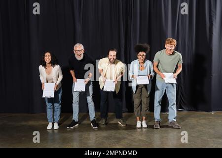 excited actors with bearded screenwriter looking at camera and laughing on stage in theater Stock Photo