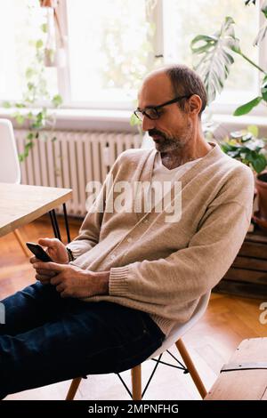 Man using smart phone while sitting on chair at home Stock Photo