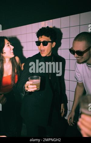 Cheerful non-binary person enjoying dance with friends against wall at nightclub Stock Photo