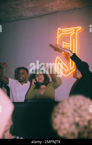 Happy young female DJ amidst friends enjoying at nightclub Stock Photo