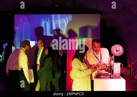 Male and female entrepreneurs discussing over 3D printer with colleagues in background at convention center Stock Photo