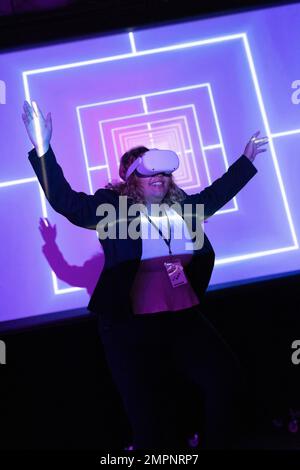 Happy businesswoman wearing VR glasses standing with arms raised in convention center Stock Photo