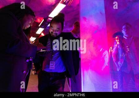 Smiling female entrepreneur sharing smart phone with male colleague at illuminated convention center Stock Photo