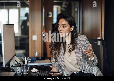 Female entrepreneur looking at computer while talking on smart phone at office Stock Photo