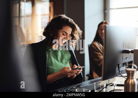 Happy female entrepreneur using mobile phone sitting at desk in office Stock Photo