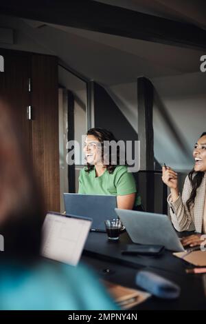 Mature business colleagues with laptops laughing while sitting at desk in office meeting Stock Photo