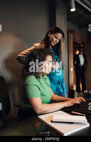 Businesswoman working on laptop by female pregnant colleague in office Stock Photo