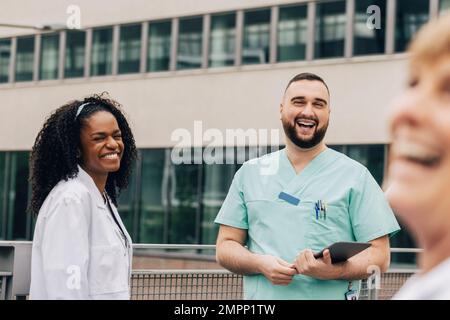 Cheerful male and female healthcare workers standing outside hospital Stock Photo