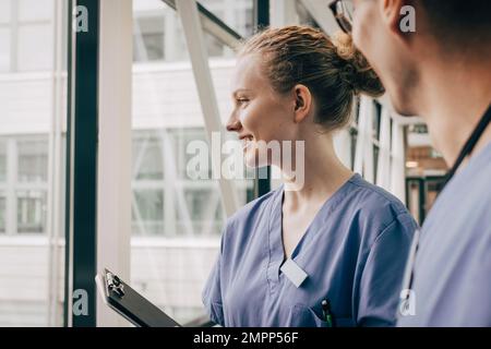 Smiling female nurse looking through window at hospital Stock Photo