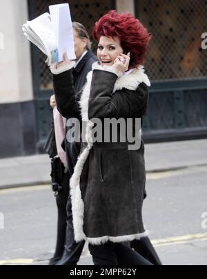 Wearing a shearling jacket and showing off her fire-engine red hair, Brazilian UK-based comedy actress and TV presenter Cleo Rocos (aka Cleopatra Rocos) is all smiles as she waves to photographers while chatting on her cellphone. London, UK. 01/24/11. Stock Photo