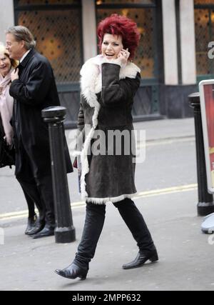 Wearing a shearling jacket and showing off her fire-engine red hair, Brazilian UK-based comedy actress and TV presenter Cleo Rocos (aka Cleopatra Rocos) is all smiles as she waves to photographers while chatting on her cellphone. London, UK. 01/24/11. Stock Photo