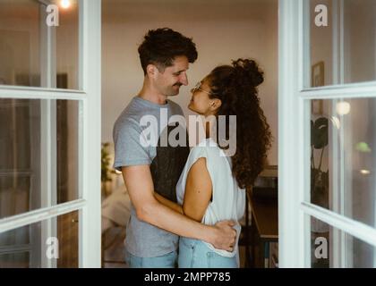 Side view of smiling couple looking at each other seen through doorway Stock Photo