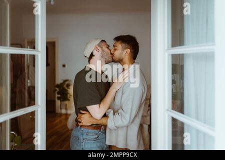 Side view of romantic gay couple kissing each other seen through doorway Stock Photo