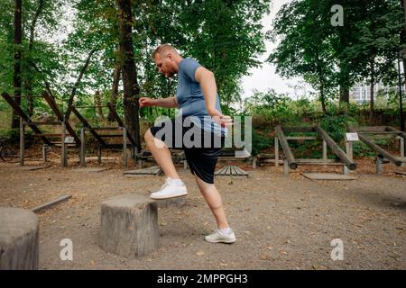 Side view of dedicated overweight man exercising on tree stump at park Stock Photo