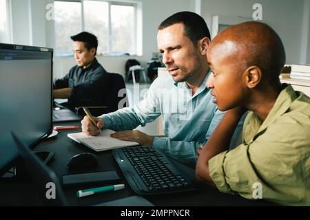 Businesswoman discussing with male colleague taking down notes while looking at computer in office Stock Photo