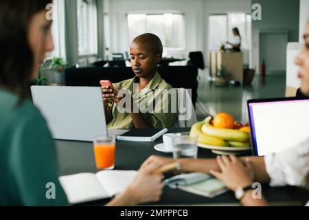 Businesswoman with shaved head using smart phone while sitting in office Stock Photo